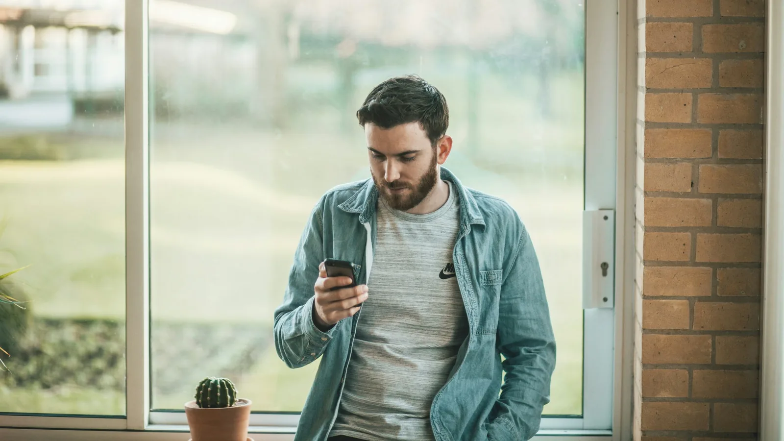 Homem consultando um smartphone junto à janela, imagem ilustrativa da revisão de uma conta de namoro