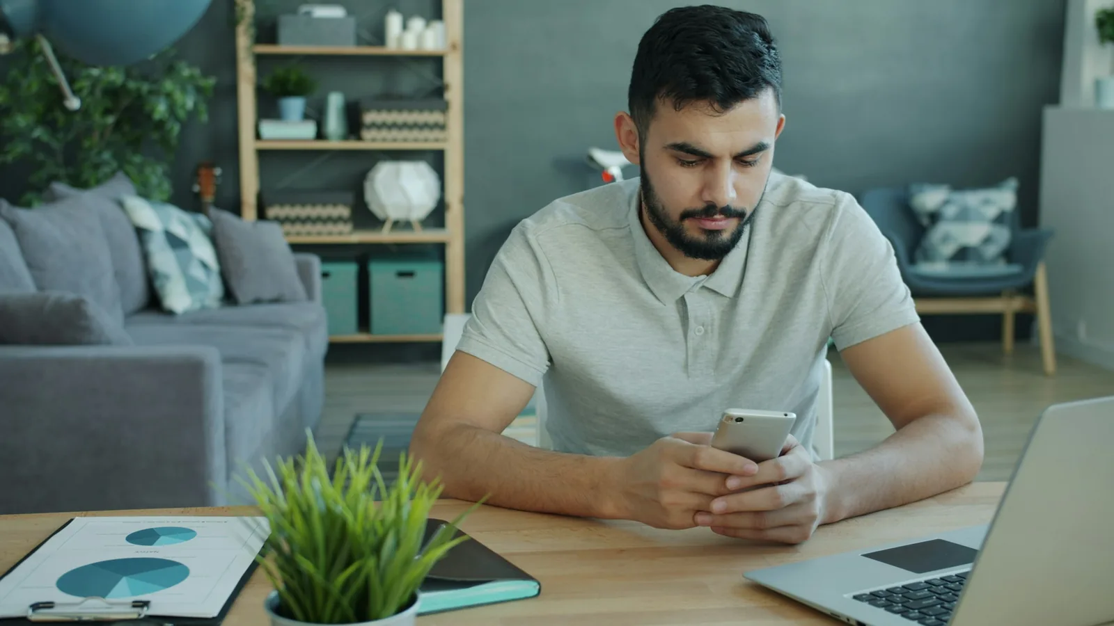 Homem conferindo o celular ao lado de um notebook, imagem ilustrativa de organização antes de excluir uma conta