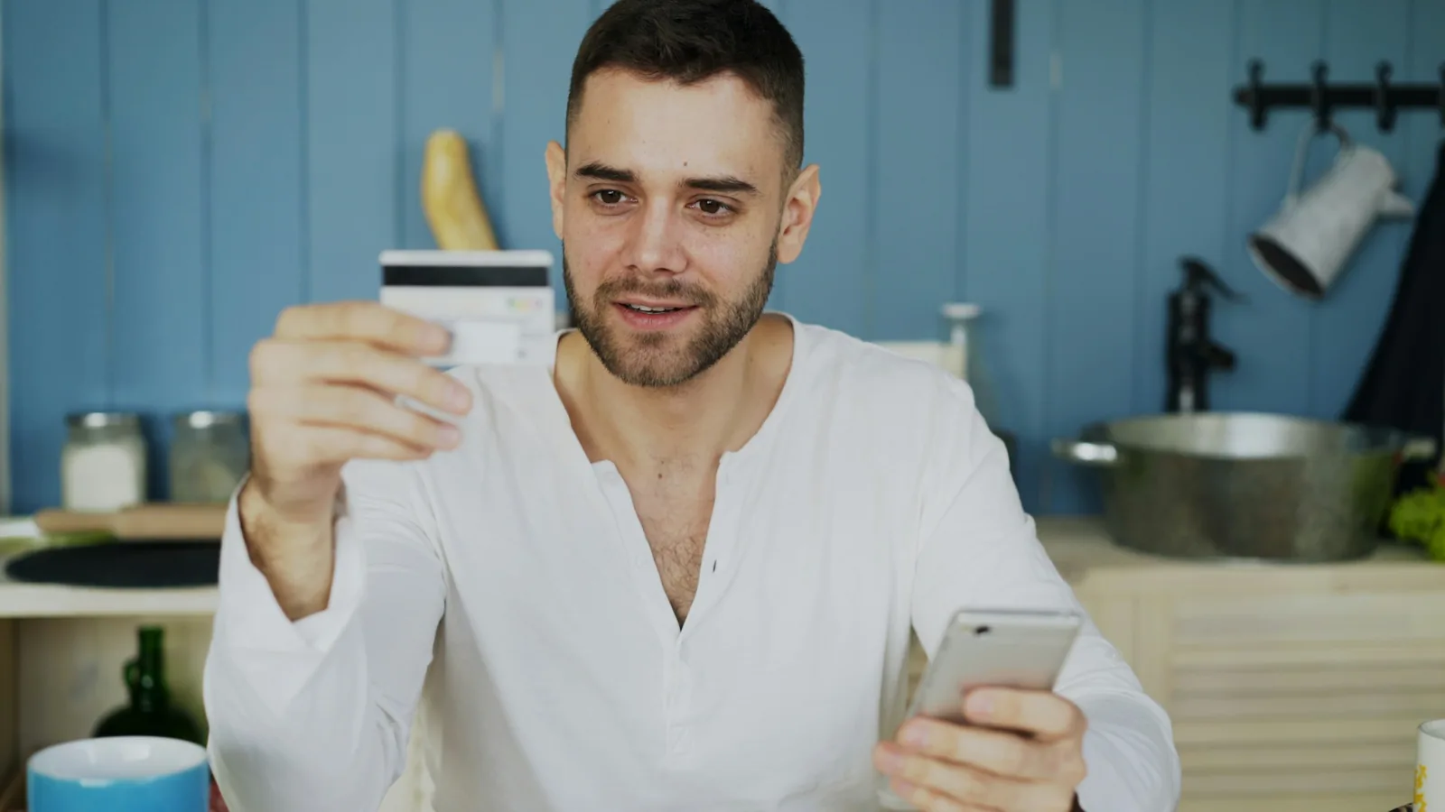 Homem com cartão e celular à mesa, imagem ilustrativa da conferência de uma assinatura de aplicativo