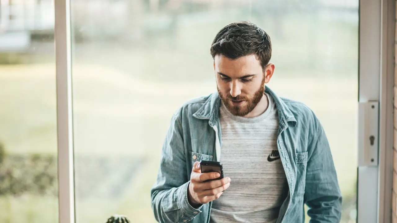 Homem lendo mensagem no celular perto da janela durante uma conversa de paquera pelo direct